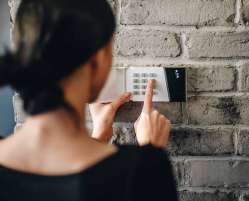 Young woman entering security pin on home alarm keypad_